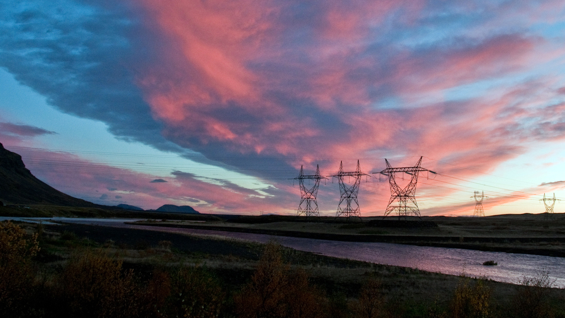 Forsíðumynd: Rafmagnsmöstur við fljót í sólarlaginu.